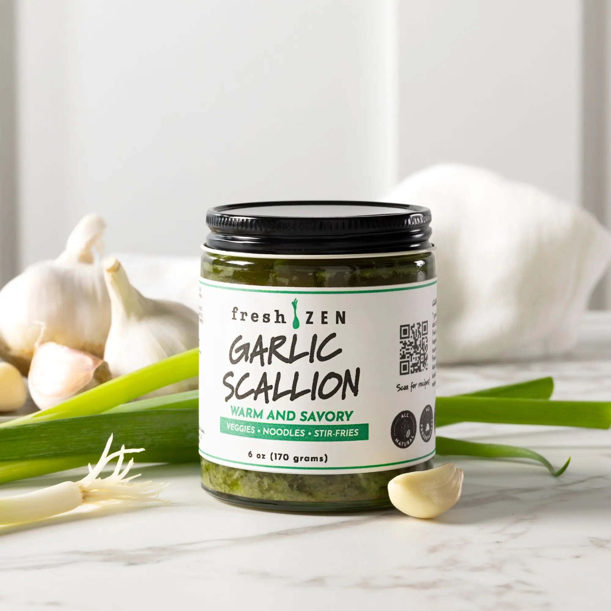 Jar of Fresh Zen Garlic Scallion sauce on a marble surface with garlic and scallions and garlic around