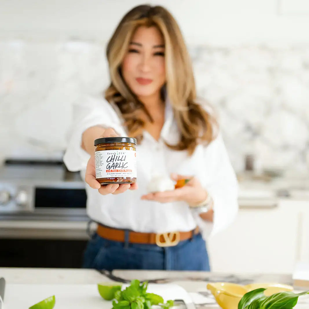 Fresh Zen founder, ruby Chan holding a jar of chili garlic sauce in a kitchen setting