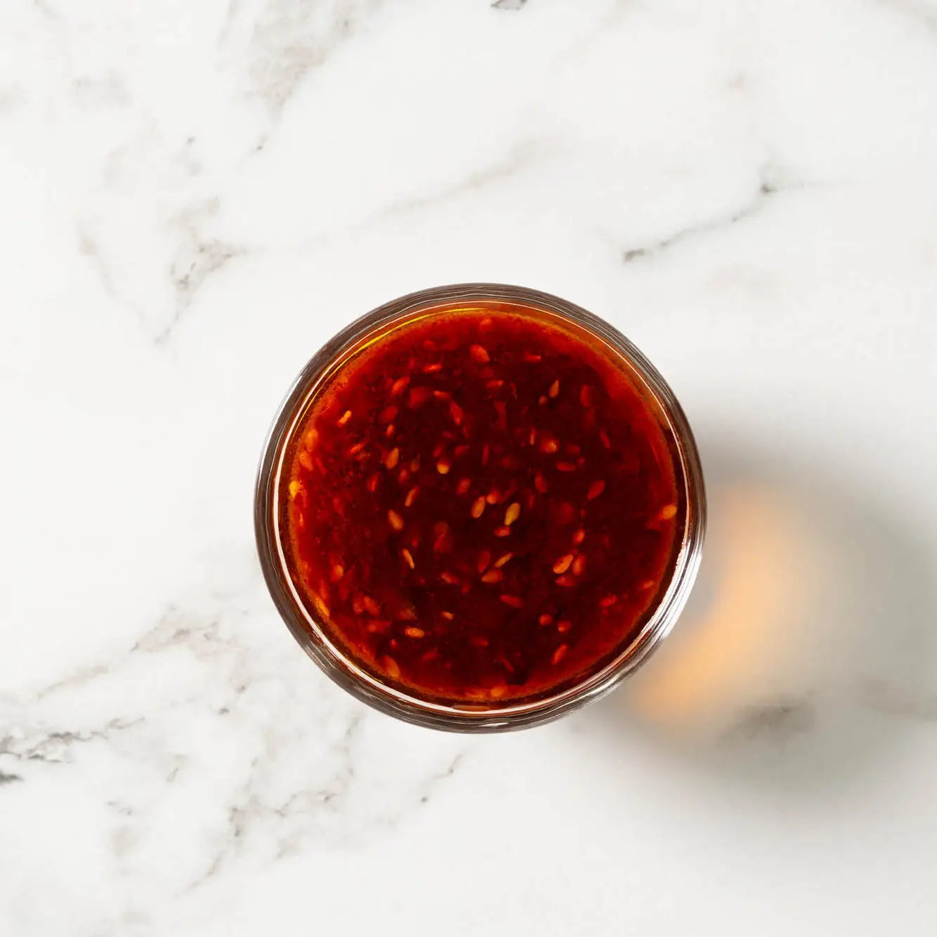 A clear glass jar of korean chili crunch sauce filled with vibrant red chili sauce speckled with sesame seeds