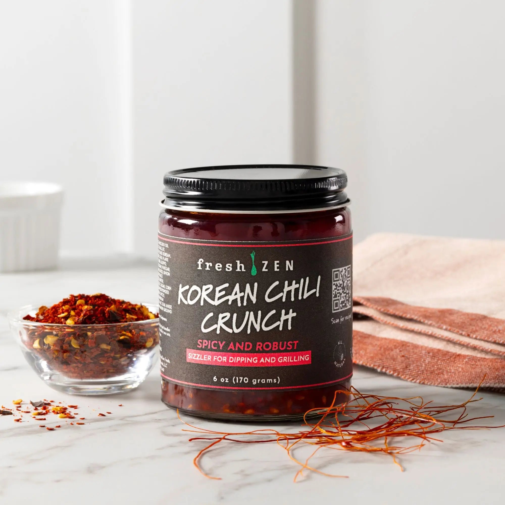 Jar of Fresh Zen Korean Chili Crunch sauce on a marble surface with chili flakes and a towel.
